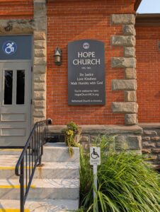 Grey sign on brick building with Micah 6:8 verse from Bible, also shows accessible entrance sign